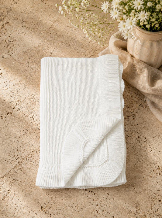 White ribbed blanket on a textured surface with a vase of flowers.