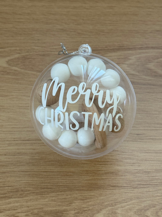 Clear ornament with 'Merry Christmas' text and white teether on a wooden surface
