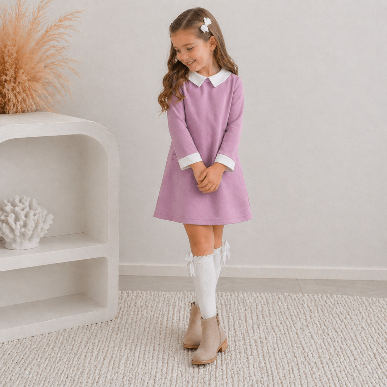 7 yr old girl in the Ariella winter dress paired with knee high white socks with cream ankle boots. She's posing and smiling, standing on white carpet.