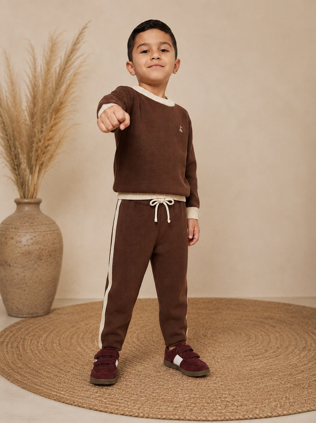 Toddler Boy wearing a brown sweater and pants standing on a beige rug with a vase in the background