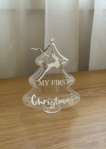 Clear Christmas tree ornament with 'My First Christmas' text on a wooden surface.
