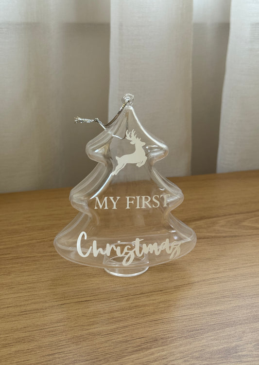 Clear Christmas tree ornament with 'My First Christmas' text on a wooden surface.