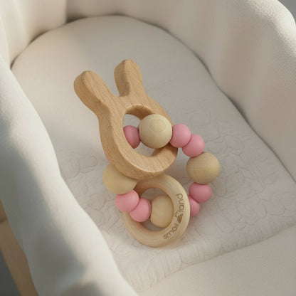 Wooden bunny teething ring with pink silicon beads on a soft beige surface