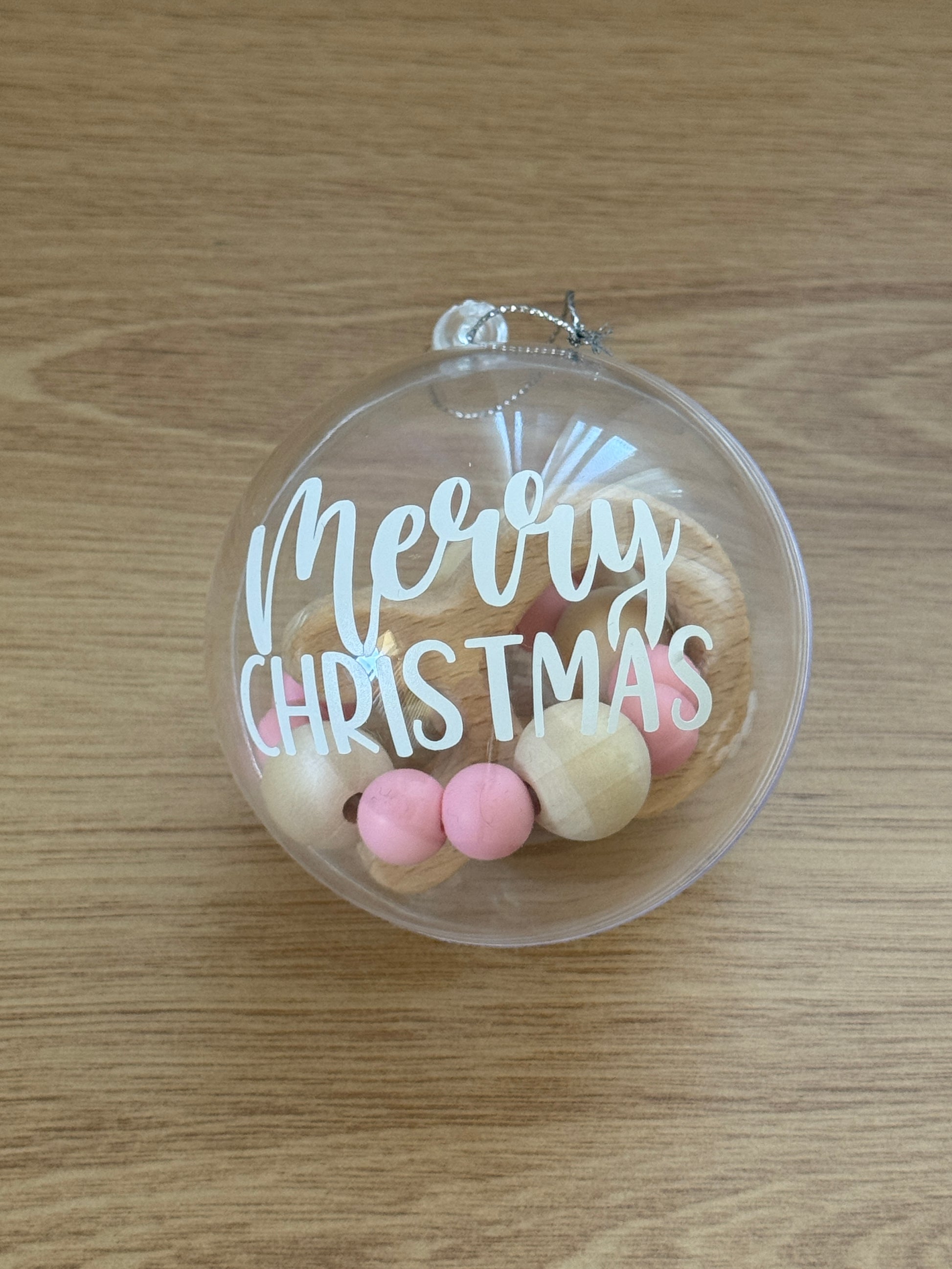 Clear Christmas ornament with 'Merry Christmas' text and bunny teether on a wooden surface