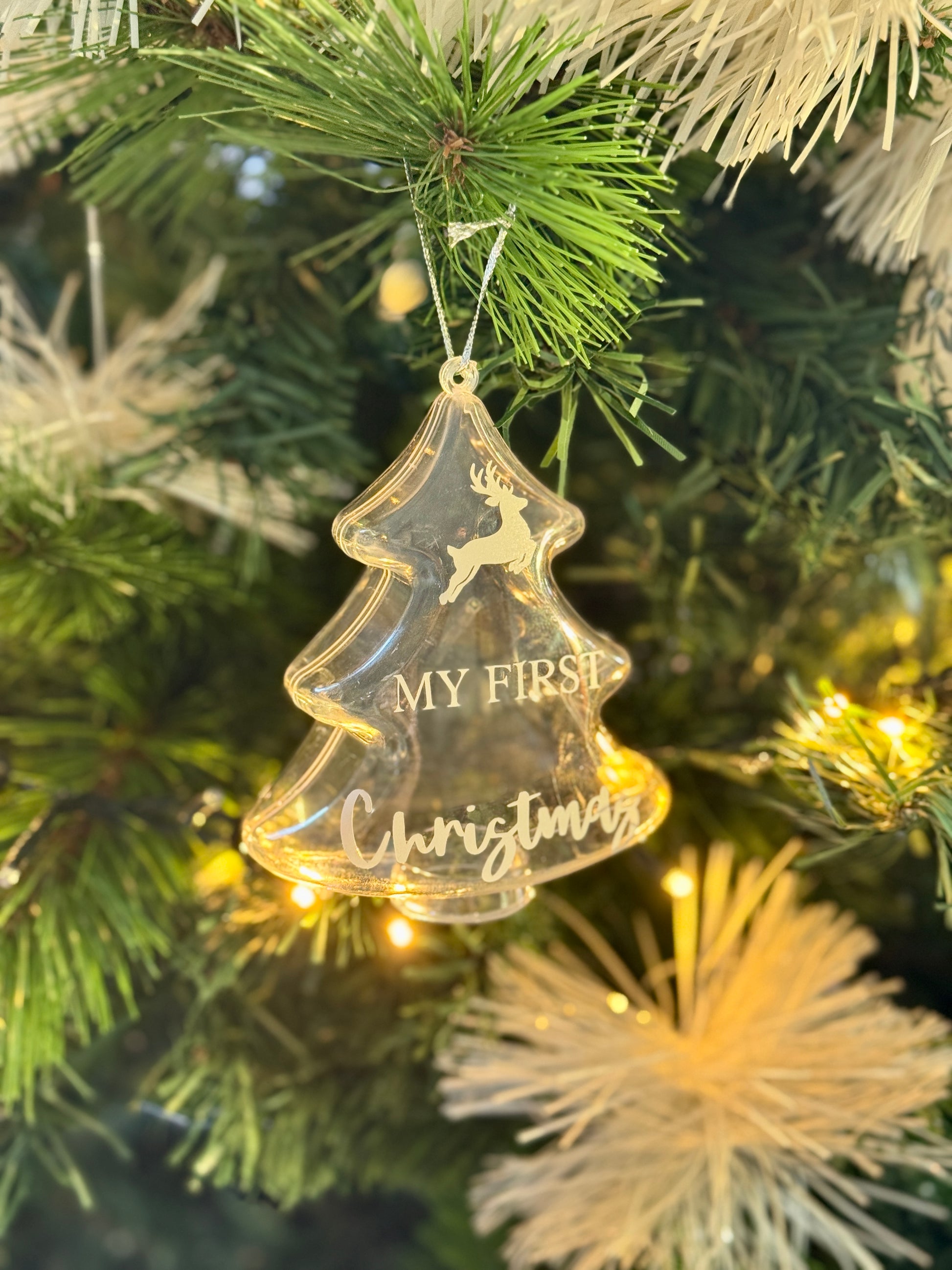 white text saying "My First Christmas" on a Christmas tree clear Ornament hanging on a Christmas tree