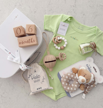 Baby clothing and toys including a lime onesie, wooden blocks, and a plush teddy toy on a light surface.