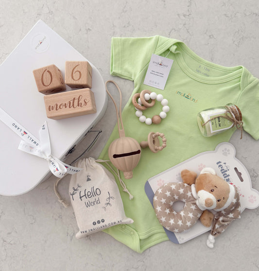 Baby clothing and toys including a lime onesie, wooden blocks, and a plush teddy toy on a light surface.