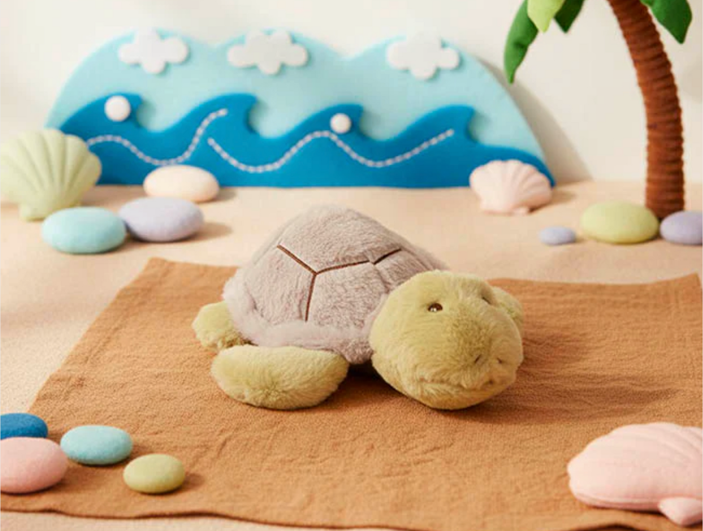 Plush turtle toy on a sandy surface with a decorative ocean scene in the background.