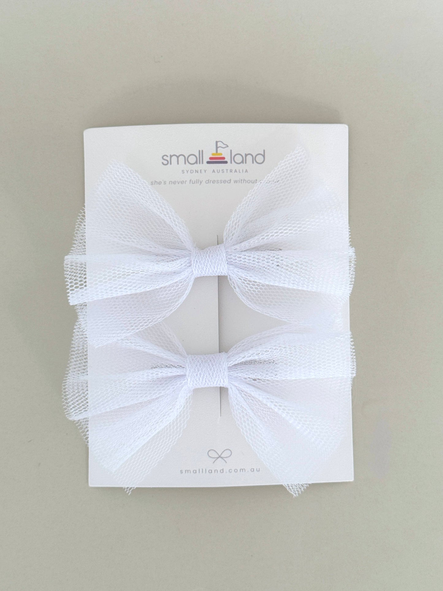 Two hair bow clips in white, displayed on a flat surface with packaging cards behind them.