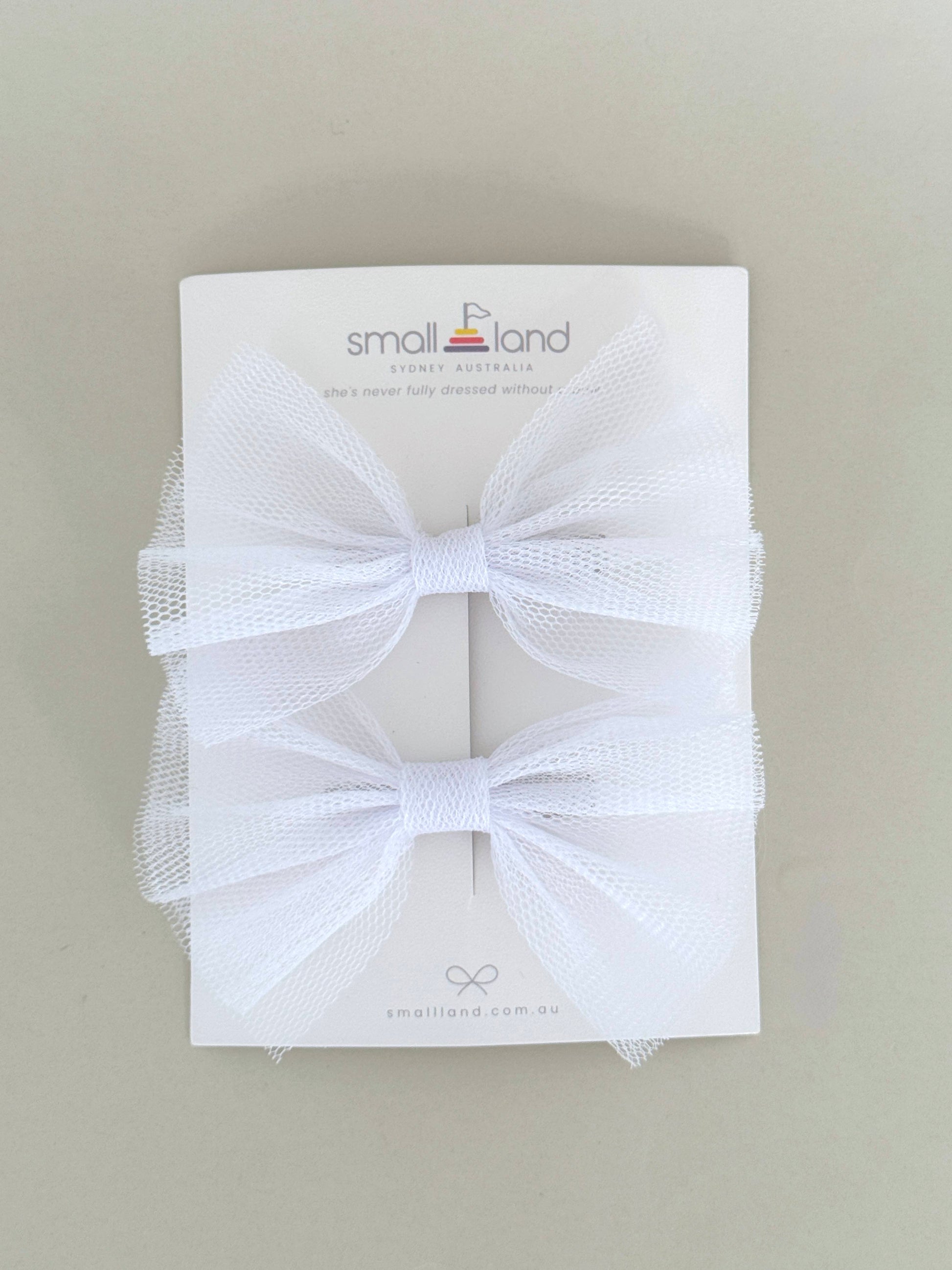 Two hair bow clips in white, displayed on a flat surface with packaging cards behind them.