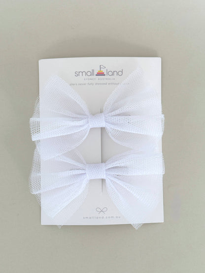 Two hair bow clips in white, displayed on a flat surface with packaging cards behind them.
