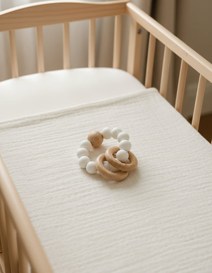 Wooden teething ring with white silicon beads on a soft beige surface