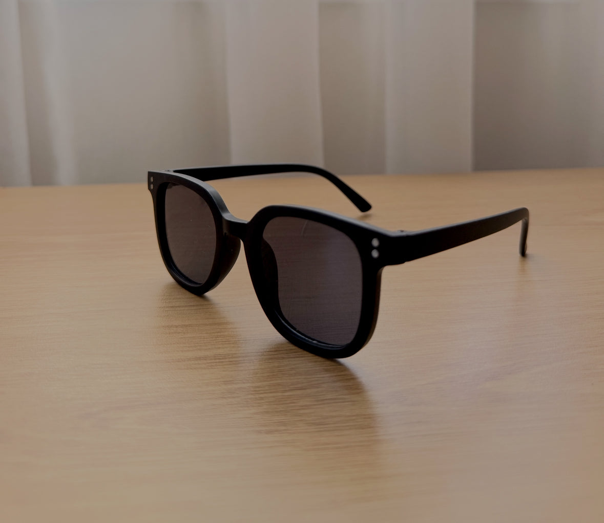 Black sunglasses on a wooden surface with a neutral background