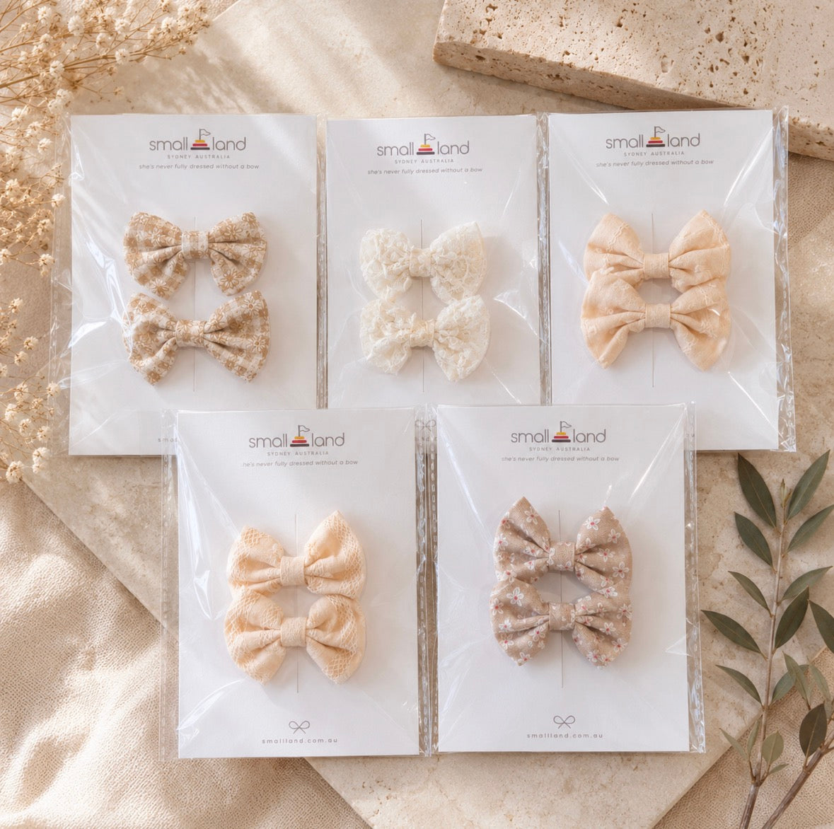 Five packages of beige mini hair bows clips, that come in 2 packs, displayed in Small Land packaging on a textured surface.