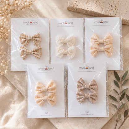 Five packages of beige mini hair bows clips, that come in 2 packs, displayed in Small Land packaging on a textured surface.