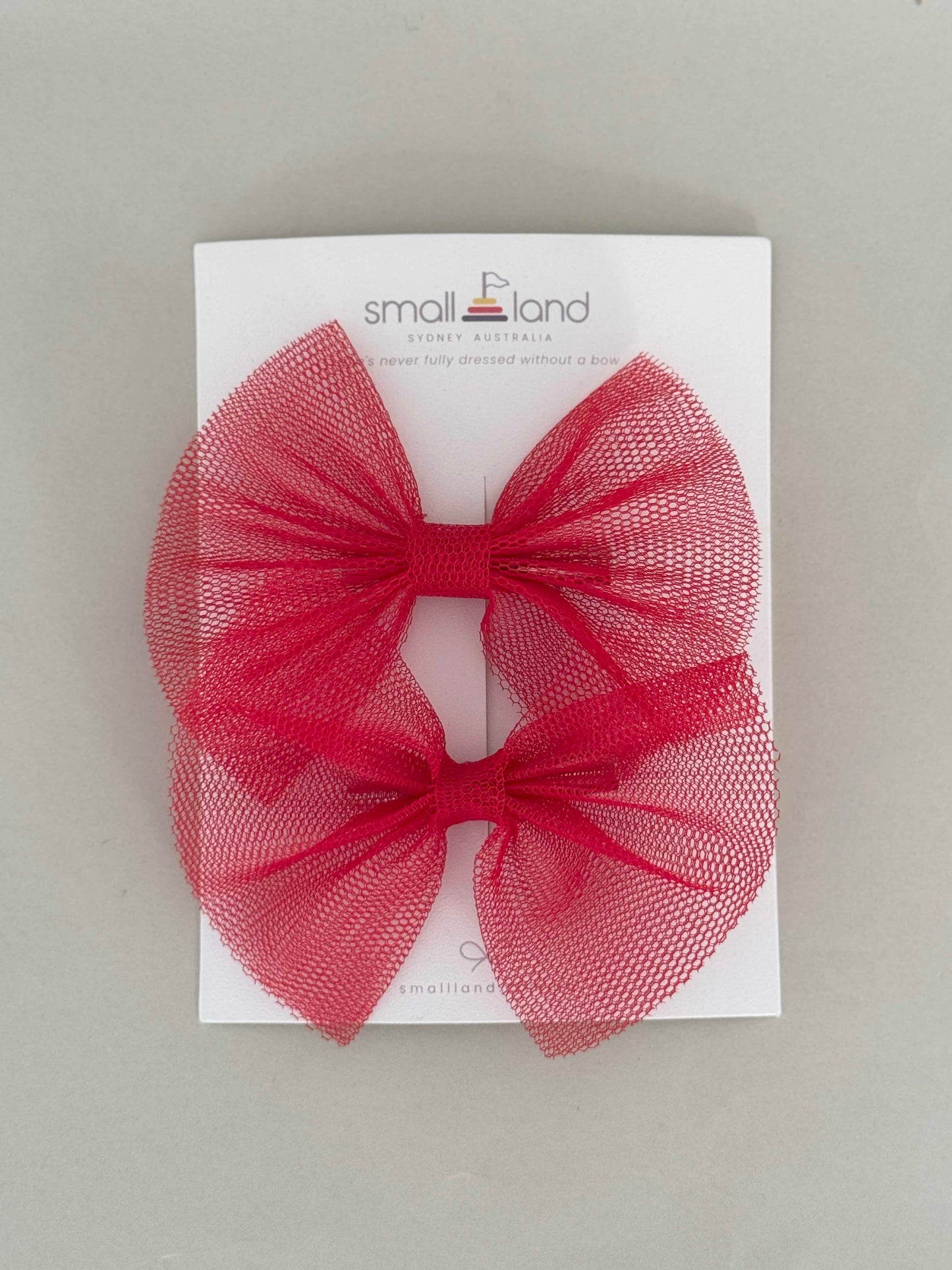 Two hair bow clips in red, displayed on a flat surface with packaging cards behind them.