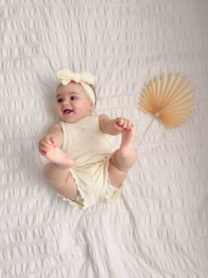 baby laying wearing cream ribbed tank top / short set with a lettuce-edge hem.