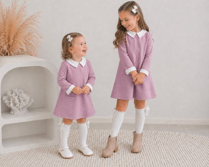 Two young girls in the Ariella winter dress paired with knee high white socks, one is wearing white mary jane shoes and the other in cream ankle boots. They're smiling, standing on white carpet.